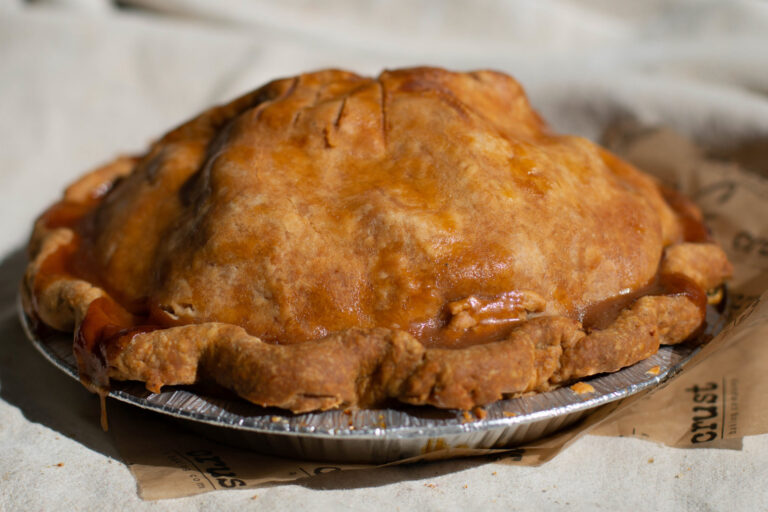 Caramel Apple Pie - CRUST - a baking company, Fenton, Michigan - Over the years, our fruit pies have quietly become legendary. Our crusts are made in-house, and each one is shaped and crimped by hand. Over three pounds of sliced apples are tucked beneath a flaky top crust, then drizzled with housemade caramel.